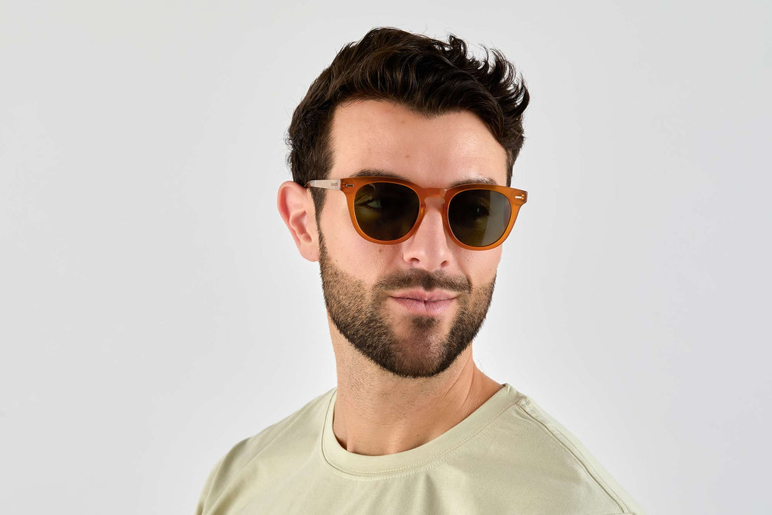 Hombre con gafas de sol redondas-cuadradas naranjas con lentes verdes polarizadas al atardecer