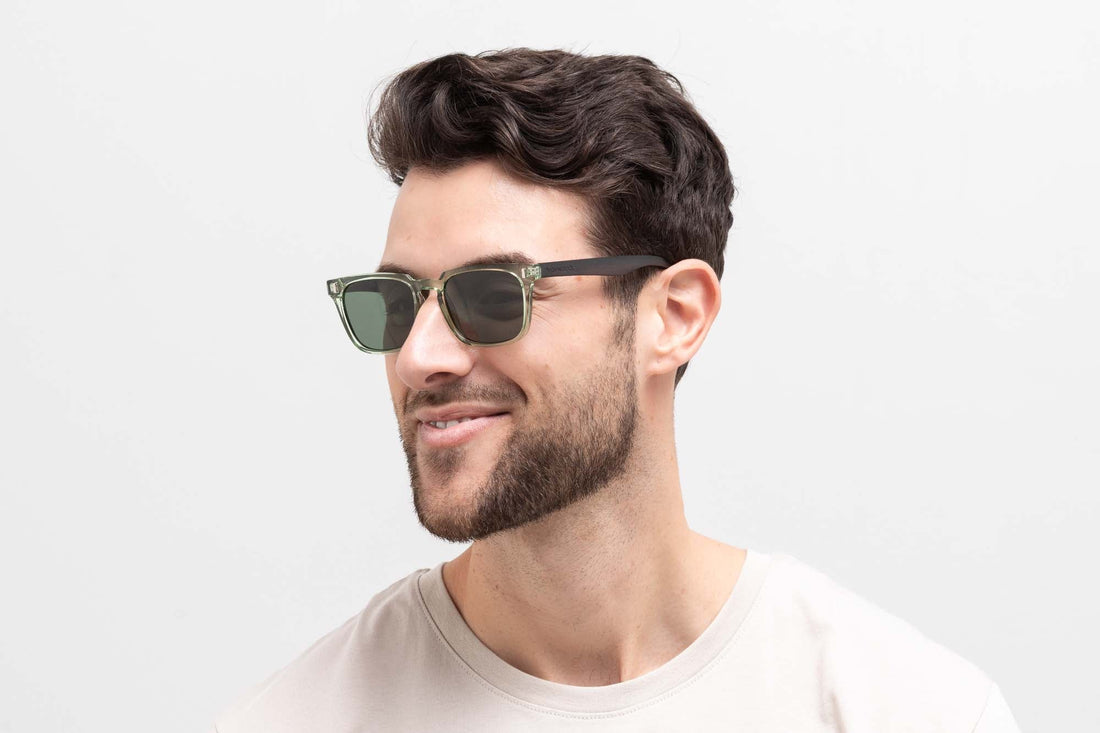 Homme portant des lunettes de soleil Oliver, des lunettes de soleil carrées vertes translucides avec des verres polarisants verts.